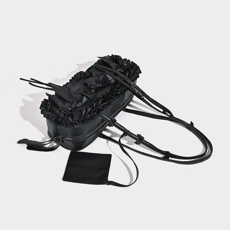 Black leather-look structured tote bag with gathered ruffle trim, ribbon bow accents, top zip closure, and attached card