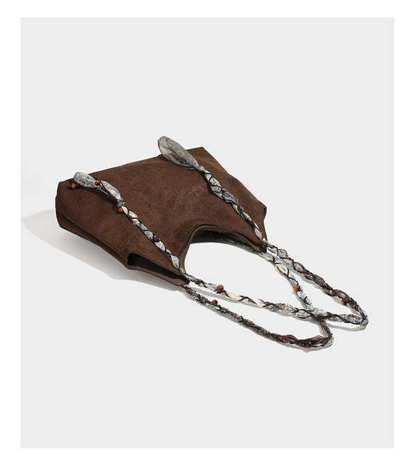 Slouchy paisley-embossed suede-look shoulder tote bag with braided patterned fabric straps and wood bead accents, detail view