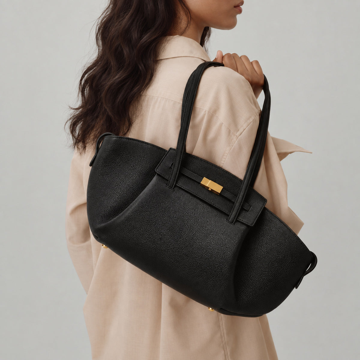 Black pebbled trapezoid tote bag with gold turn-lock hardware and double top handles, detail view 4