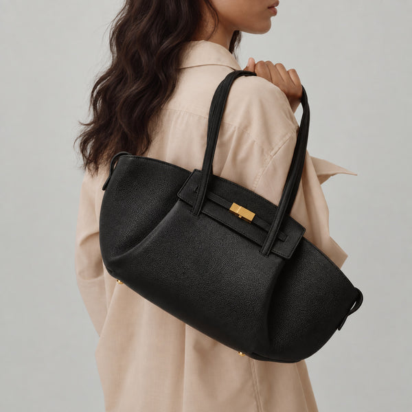 Black pebbled trapezoid tote bag with gold turn-lock hardware and double top handles, detail view 4