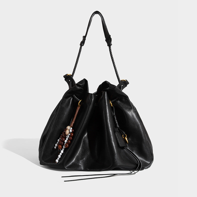 Cream slouchy drawstring bucket bag with braided cord, beaded tassel charm, and gold-tone ring hardware, detail view 4