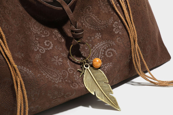 Slouchy boho hobo shoulder bag in embossed brown suede-look finish with beaded strap, cord tassels, and brass-tone leaf
