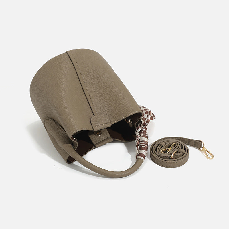 Pebbled leather-look bucket bag with checkered scarf-wrapped top handle, flap tab closure, gold-tone hardware, and matching