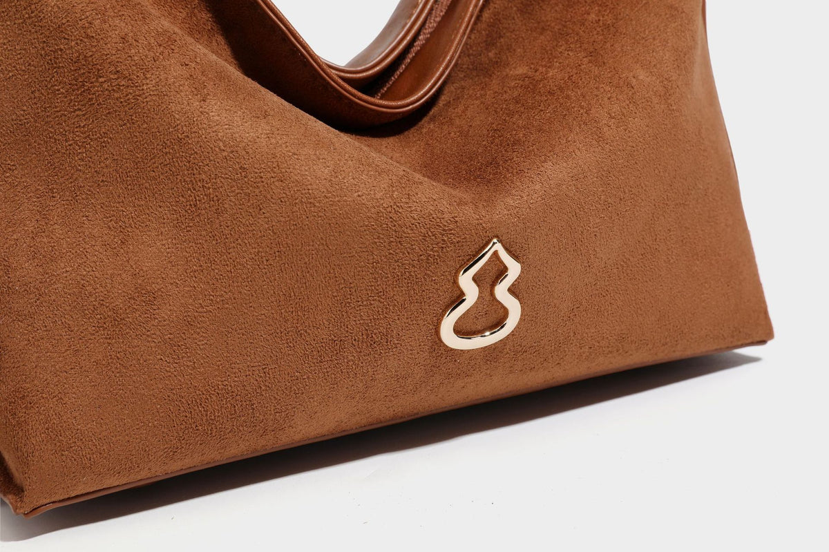 Slouchy suede-finish brown shoulder bag with long single strap and small gold-tone logo emblem on front, detail view 33