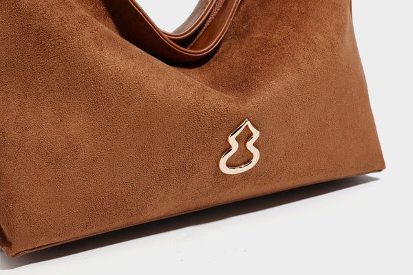 Slouchy suede-finish brown shoulder bag with long single strap and small gold-tone logo emblem on front, detail view 33