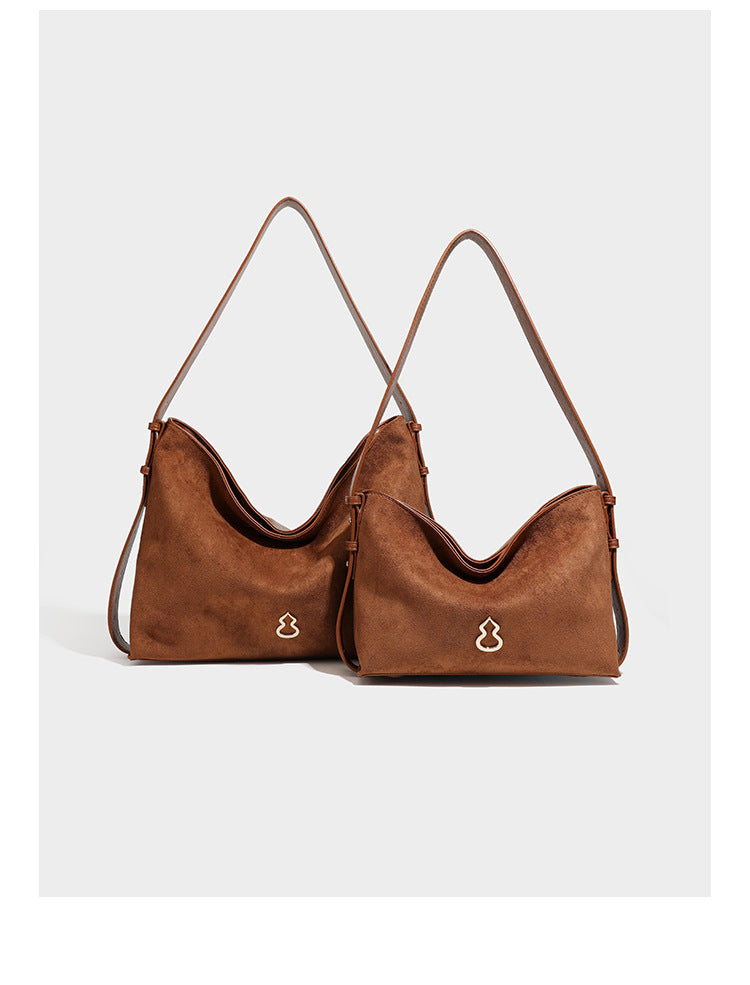 Slouchy suede-finish brown shoulder bag with long single strap and small gold-tone logo emblem on front, detail view 8