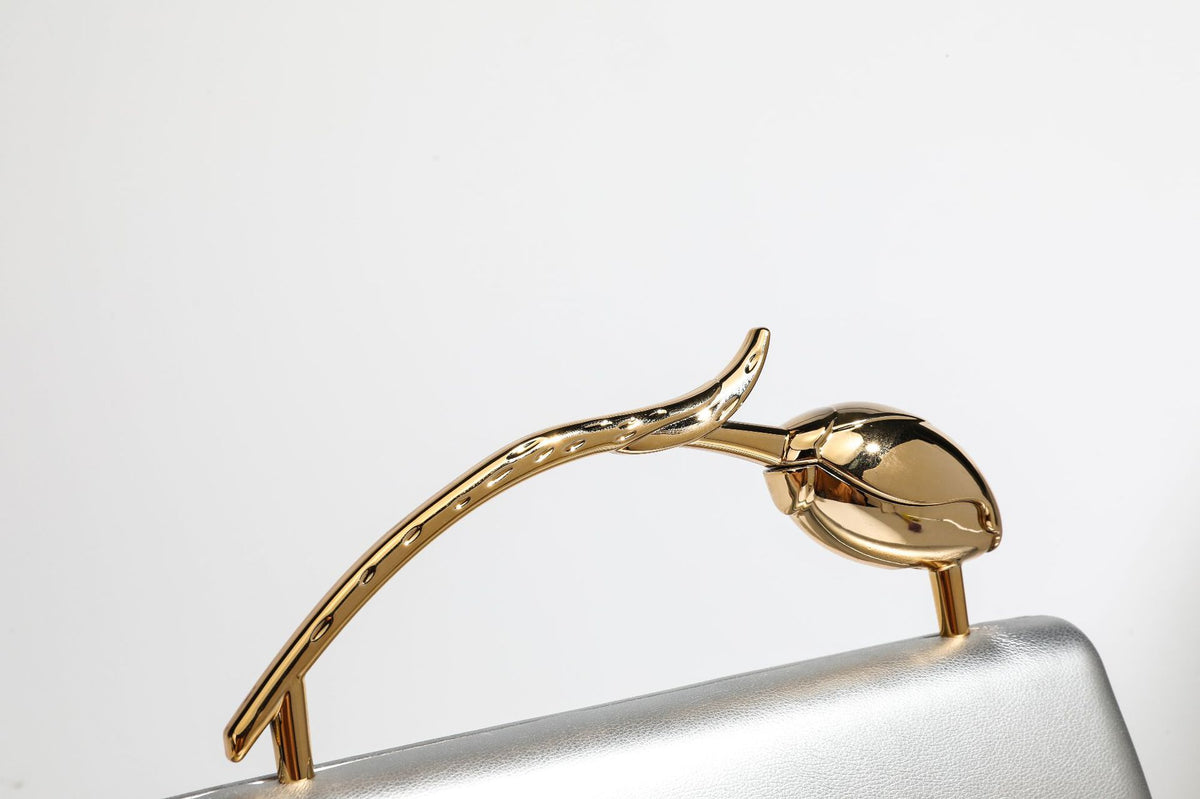 Strukturierte rechteckige Clutch mit goldfarbenem Henkel in Form einer Rosenknospe und abnehmbarem Kettenriemen in Metallic-Optik, Detailansicht