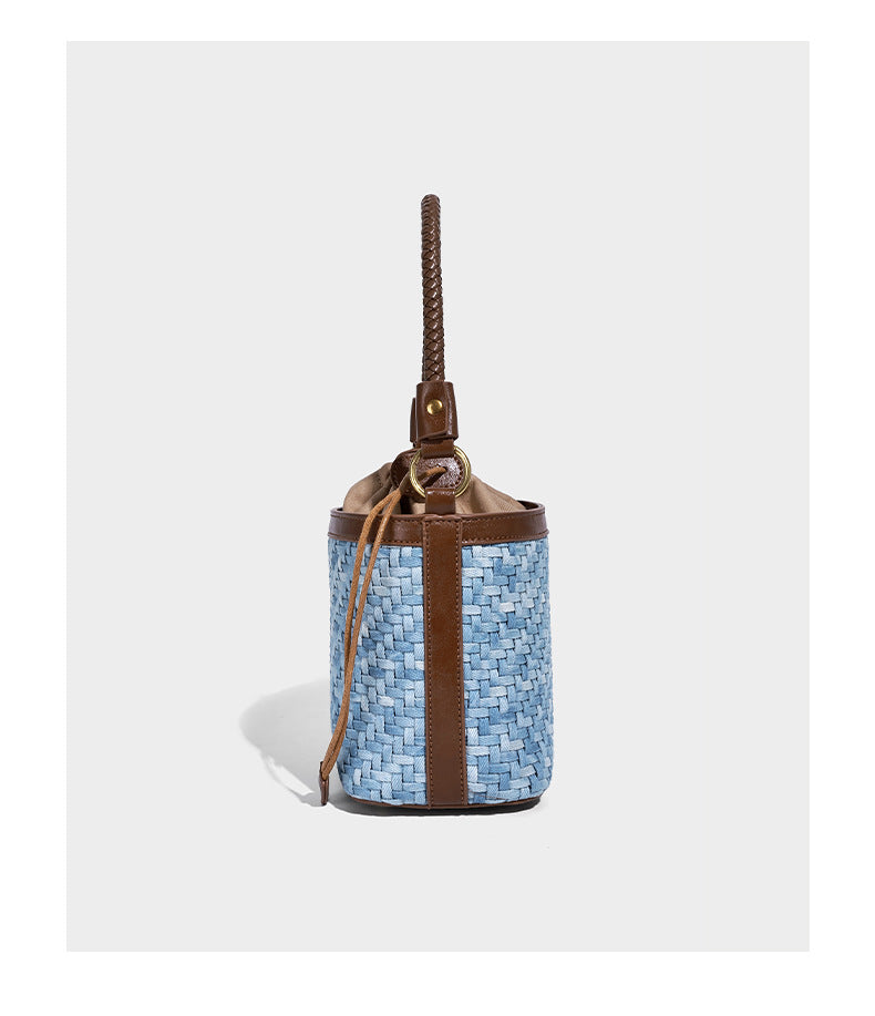 Small light blue woven bucket bag with brown leather-look trim, braided top handle, brass-tone ring hardware, drawstring
