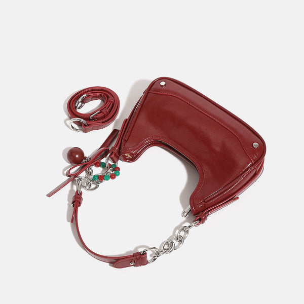 Compact crescent hobo shoulder bag in glossy burgundy leather-look finish with silver chain strap, red and green bead tassel