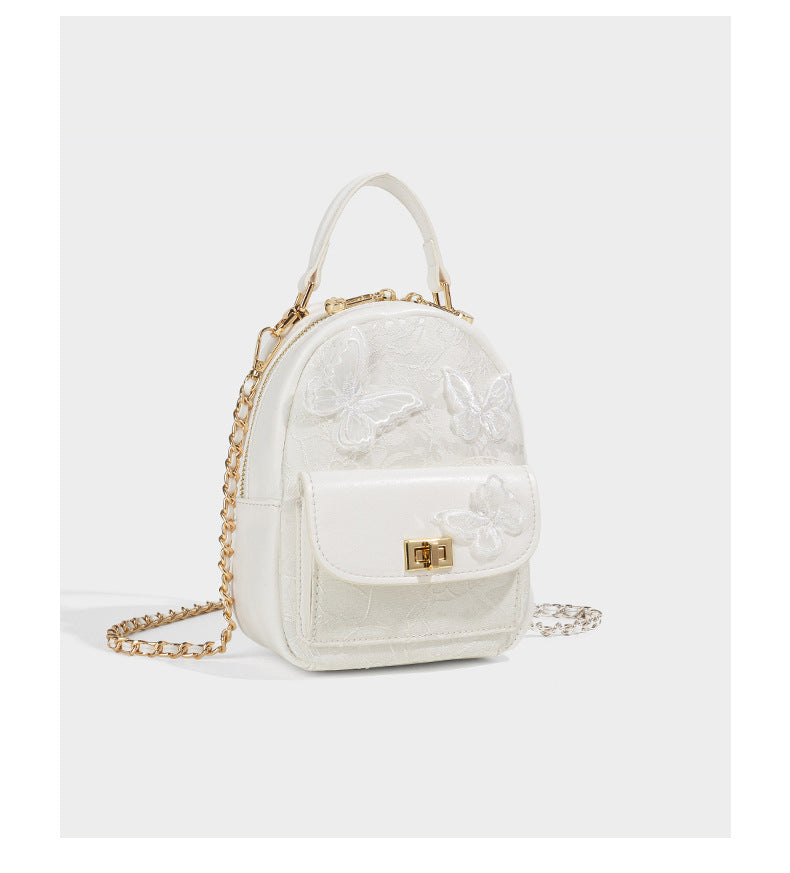 Structured mini backpack handbag with butterfly embroidery, gold-tone chain strap, and turn-lock front flap pocket, detail