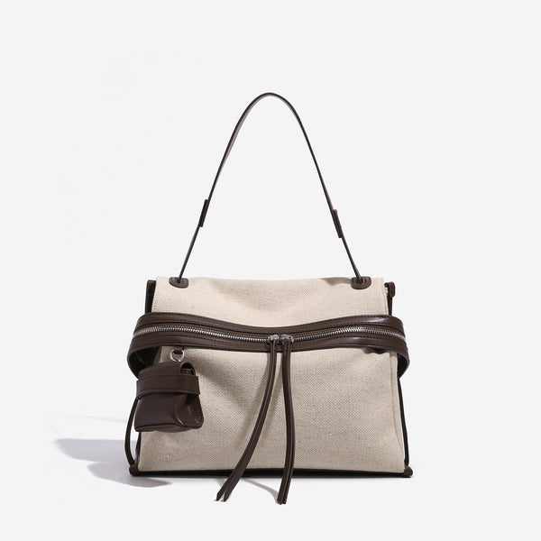 Cream canvas zip-top shoulder bag with cognac leather-look trim, dual zipper, attached mini pouch, and tassel strap ties