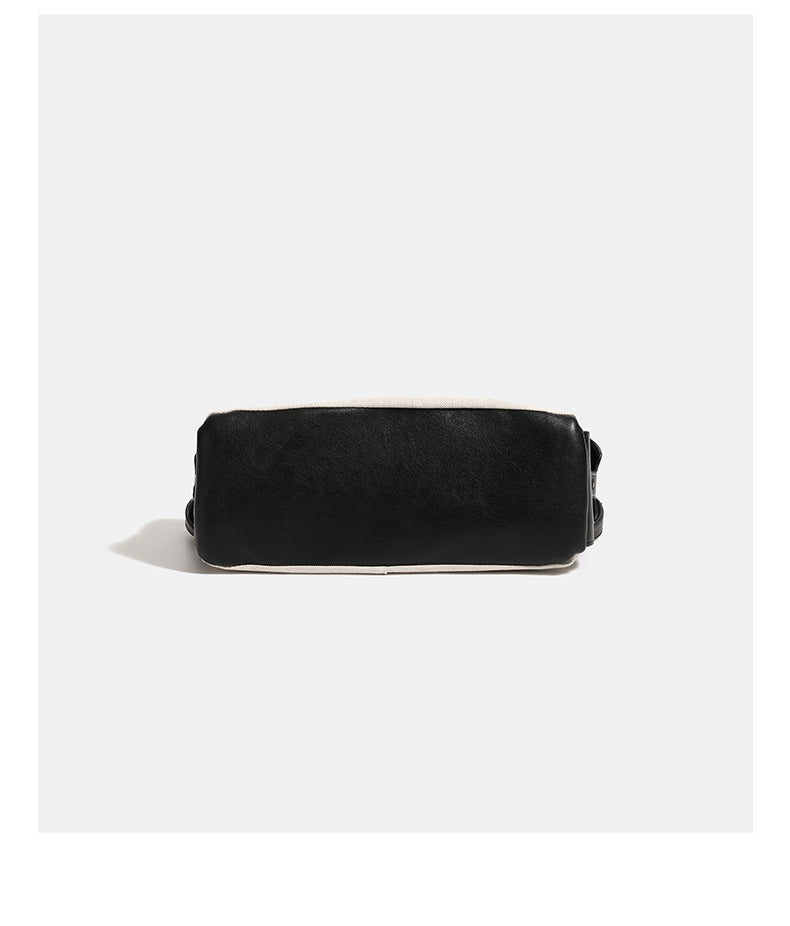Off-white canvas shoulder bag with black leather-look trim, gold-tone ring hardware, top zip closure, side flap pocket, and