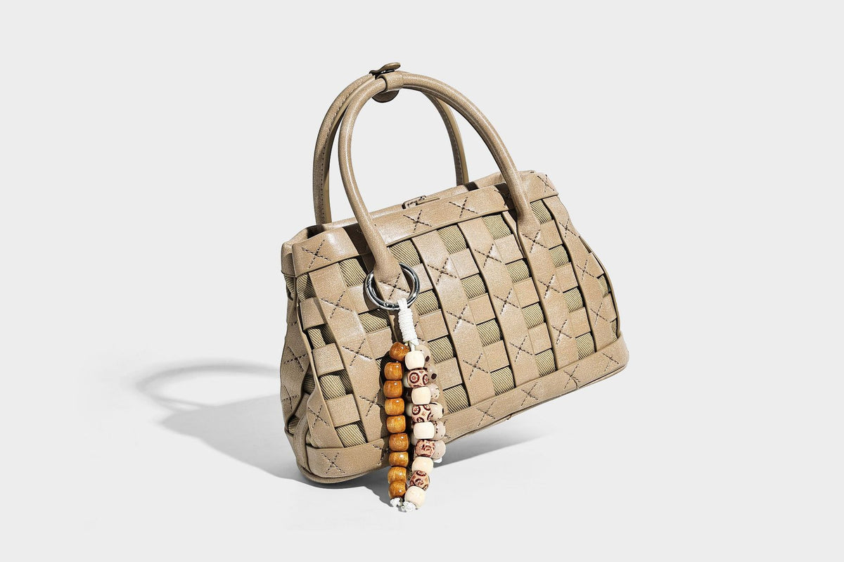 Small structured woven satchel tote with rounded top handles, silver-tone ring hardware, and bead tassel charm, detail view