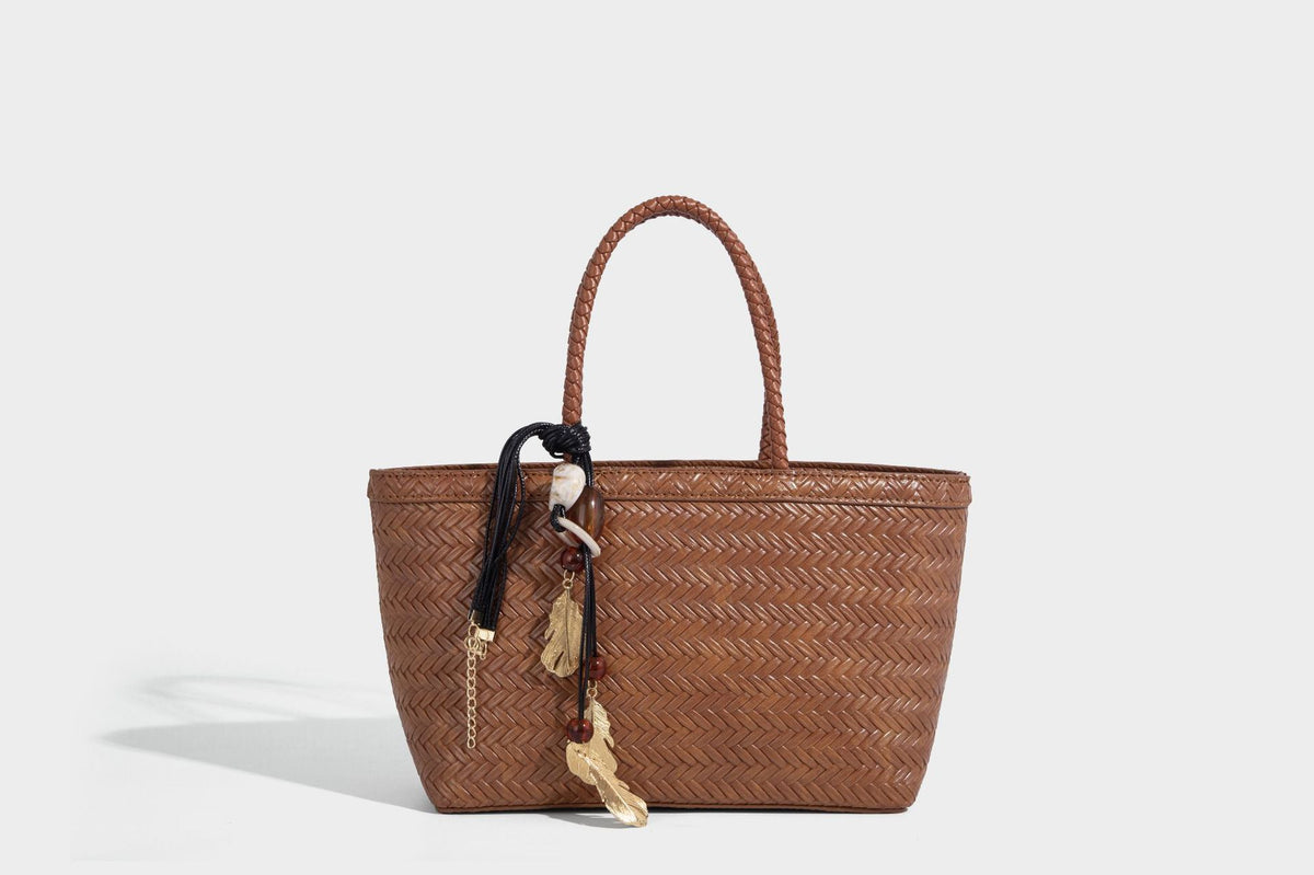 Structured chevron woven leather-look tote bag with braided top handles, gold feather charm, and adjustable shoulder strap