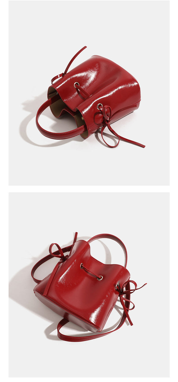 Compact glossy leather-look bucket bag with drawstring bow-tie closure, rounded top handle, and silver-tone grommet hardware