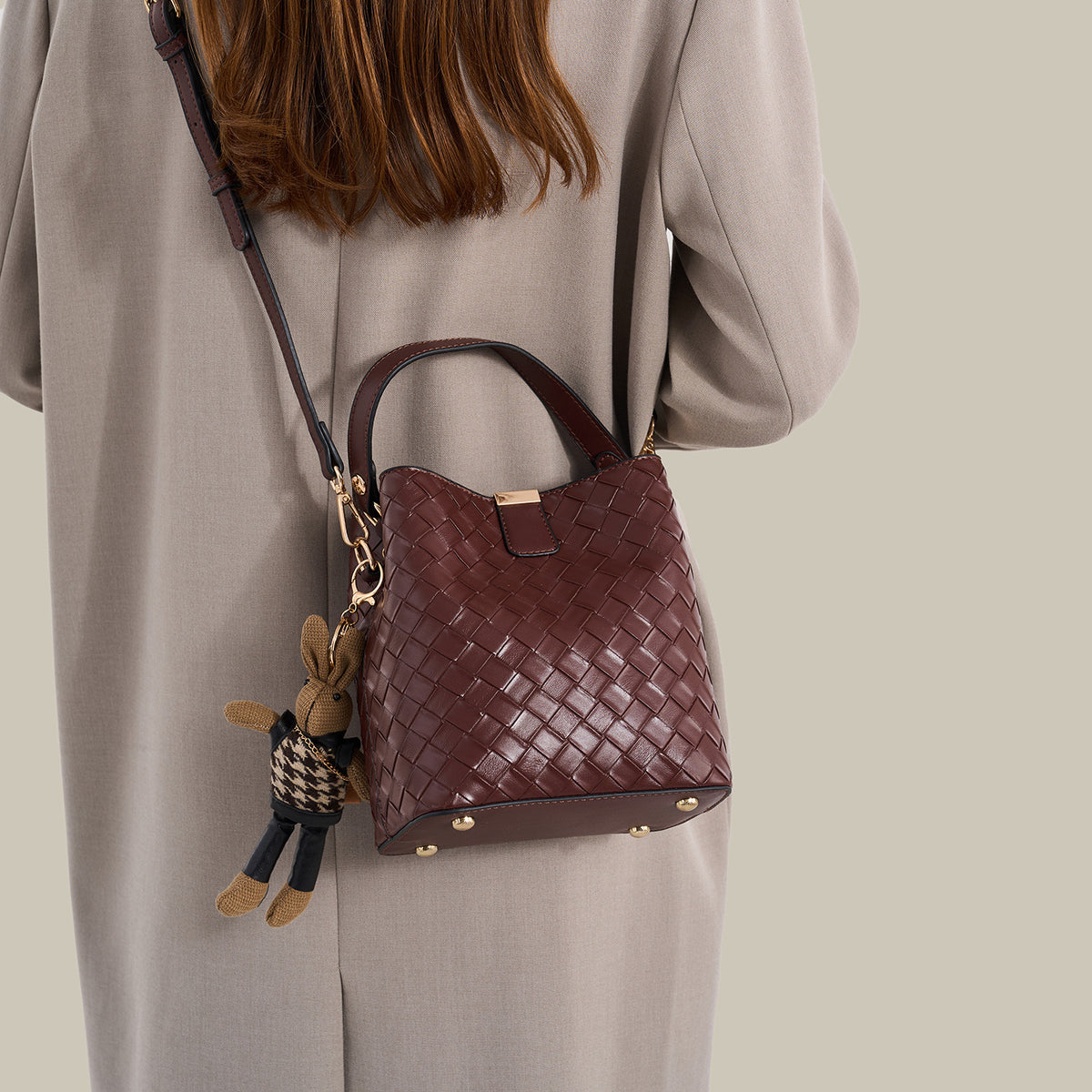Brown woven-emboss leather-look bucket bag with short top handle, detachable crossbody strap, gold-tone hardware, and rabbit