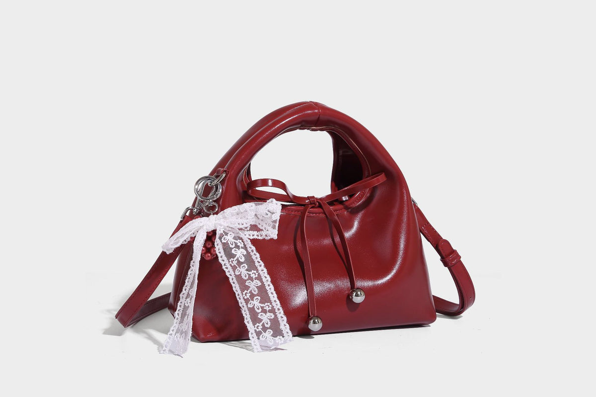 Kleine kuppelförmige Henkeltasche in glänzender Lederoptik mit Kordelzugverschluss, weißem Spitzen-Schleifenanhänger und silberfarbenen Metallbeschlägen