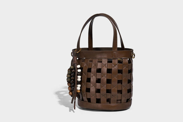 Small woven lattice bucket bag in brown leather-look finish with beaded tassel charm, dual top handles, and detachable
