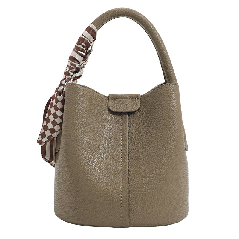 Pebbled leather-look bucket bag with checkered scarf-wrapped top handle, flap tab closure, gold-tone hardware, and matching