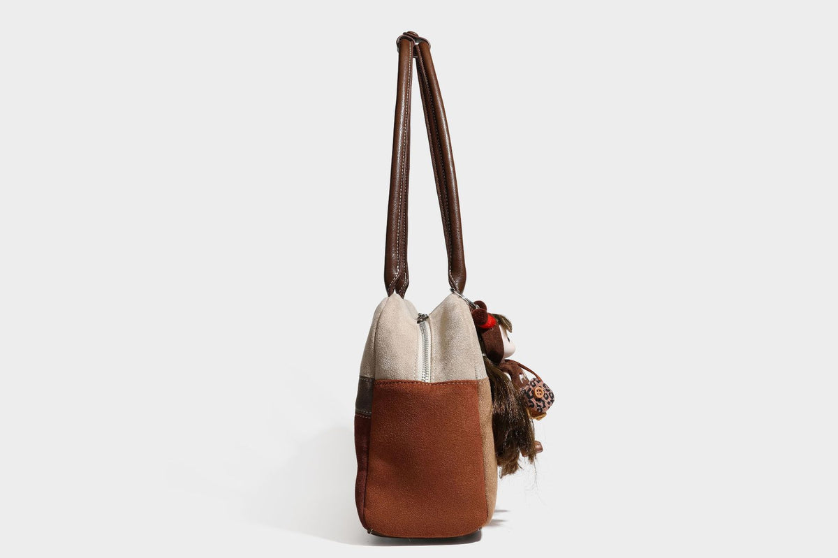 Boxy patchwork suede-look shoulder tote in tan, beige, rust, and brown panels with double brown straps and hanging doll