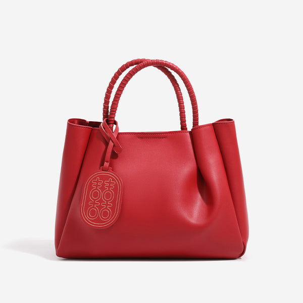 Strukturierte Tote-Bag in mattem Rot mit gedrehten, umwickelten Tragegriffen, Anhänger mit Doppelglück-Symbol und herausnehmbarem grauem Innenfach mit Reißverschluss