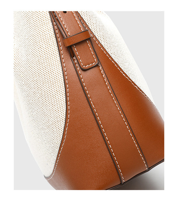 Cream canvas and tan leather-look bucket bag with arched top handle, wide detachable shoulder strap, and gold-tone hardware