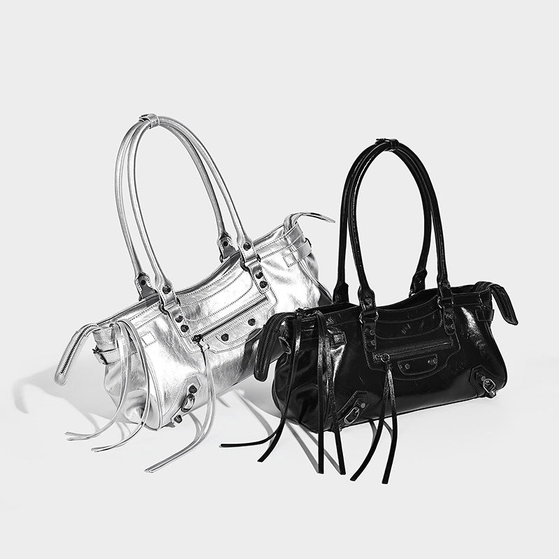 Elongated barrel shoulder bag with glossy leather-look finish, silver stud hardware, side tassels, and multiple exterior zip