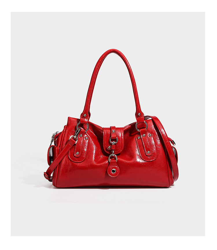 Glänzende, geknautschte Barrel-Satchel mit zwei oberen Tragegriffen, vorderem Klappen-Riemen-Panel, Ring- und Nietenbeschlägen sowie einem abnehmbaren