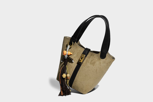 Small structured trapezoid tote bag in matte suede-look finish with black contrast trim, gold-tone front clasp, tassel charm