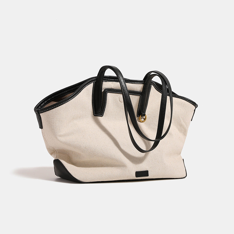 Trapezförmige Tote-Bag aus cremefarbenem Canvas mit schwarzem Besatz in Lederoptik, zwei Schulterriemen und goldfarbenen Ringbeschlägen, Detailansicht