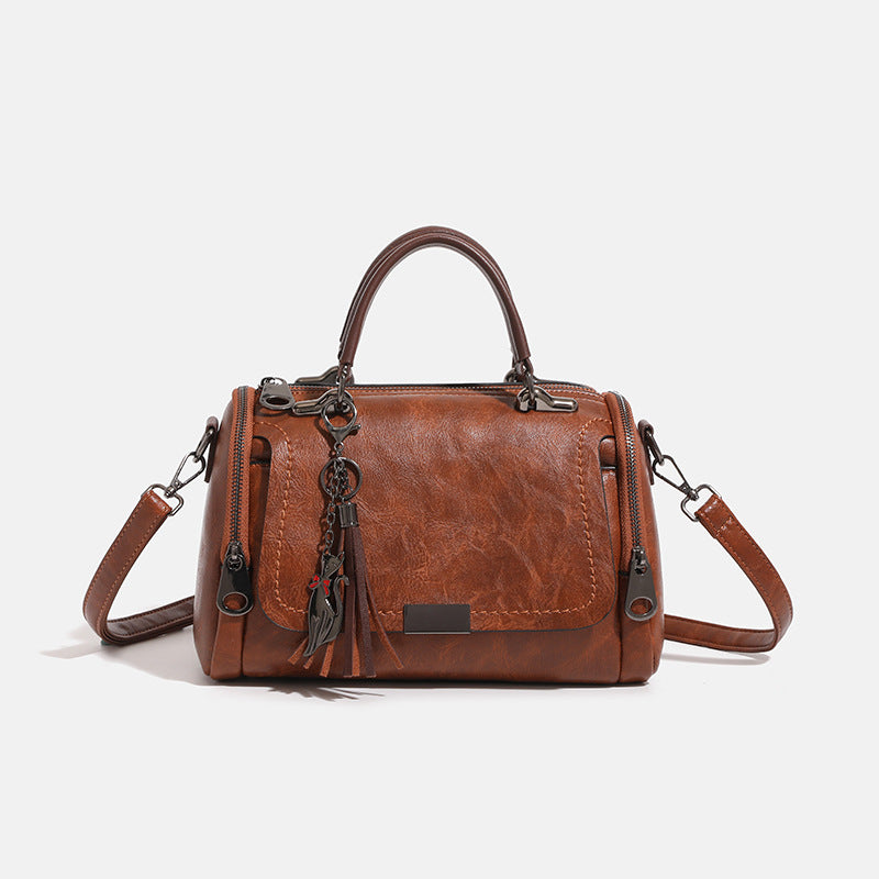 Compact structured barrel bag in distressed leather-look finish with dual top handles, detachable crossbody strap, front zip