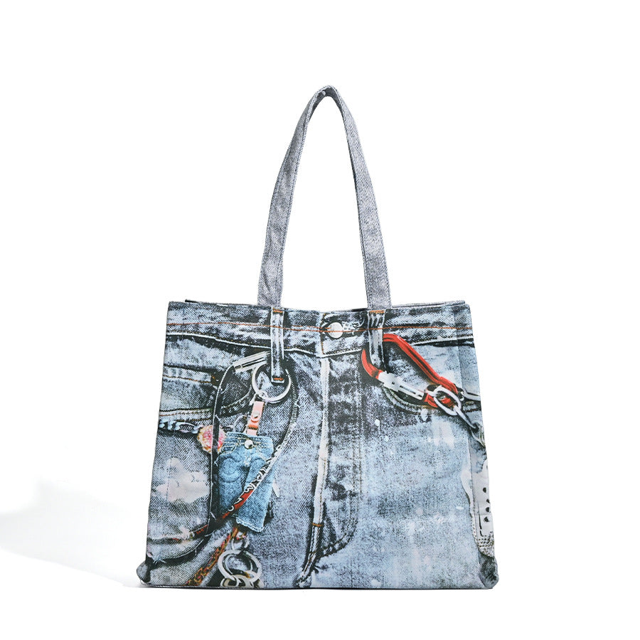 Large open-top tote bag with printed denim jeans graphic in faded blue-grey, dual flat shoulder straps and rivet hardware