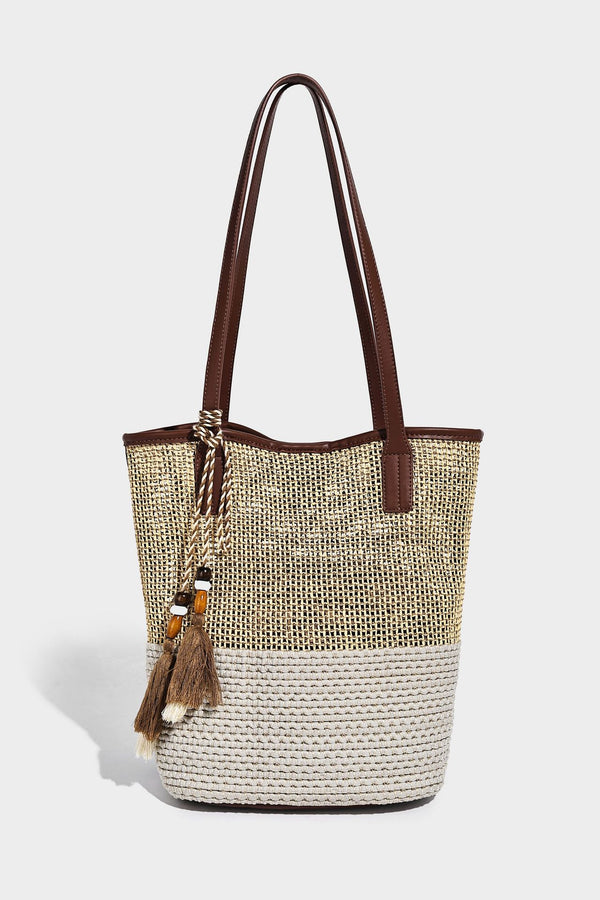 Woven straw-look tote bag in tan and cream with dark brown leather-look trim, long flat shoulder straps, and tassel bead