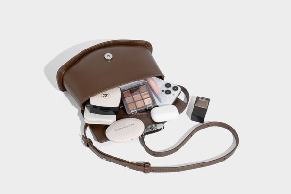 Small structured saddle bag with glossy leather-look finish, angular flap front, silver-tone metal clasp, and slim