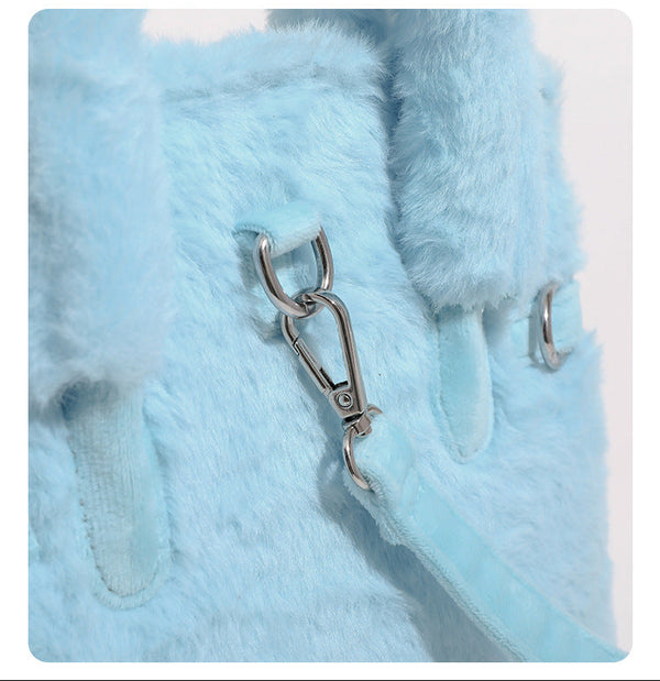 Ice-blue plush faux-fur Kelly-style convertible bag with embroidered smiling face, dark pom-pom feet, silver-tone clasp
